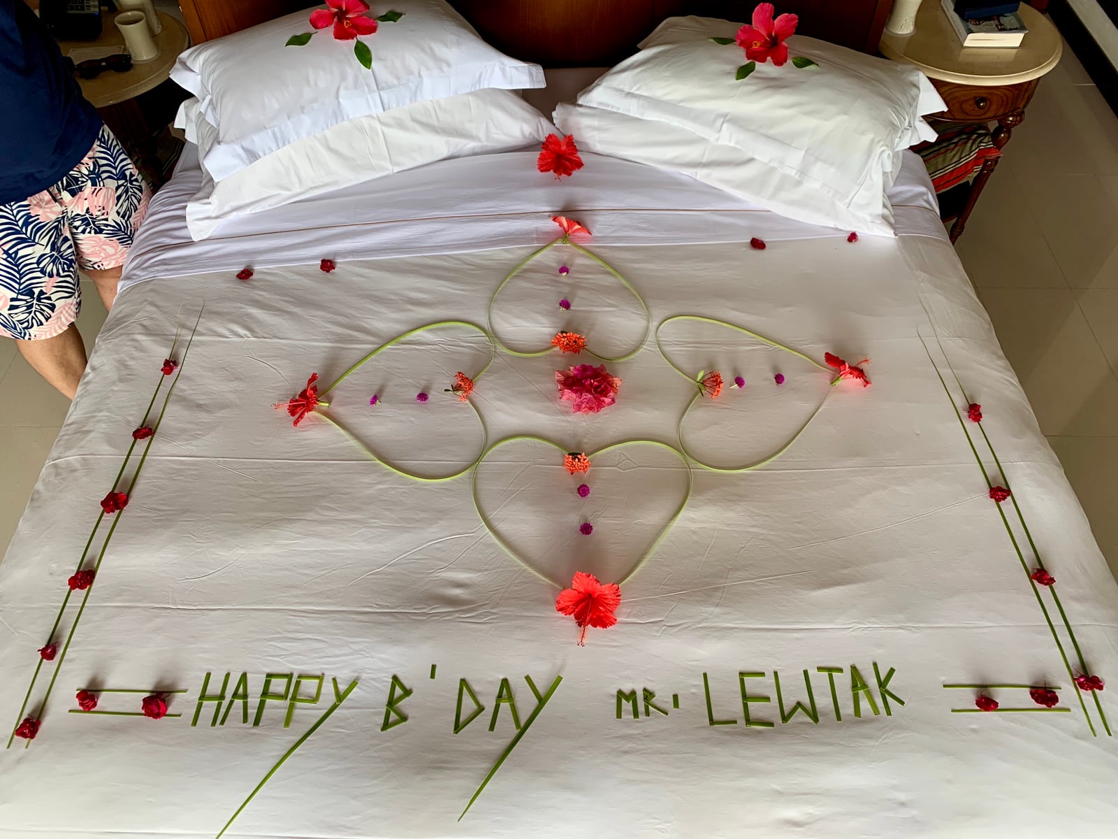 A bed dressed with petals spelling 'HAPPY B'DAY MR LEWTAK' on the sheets