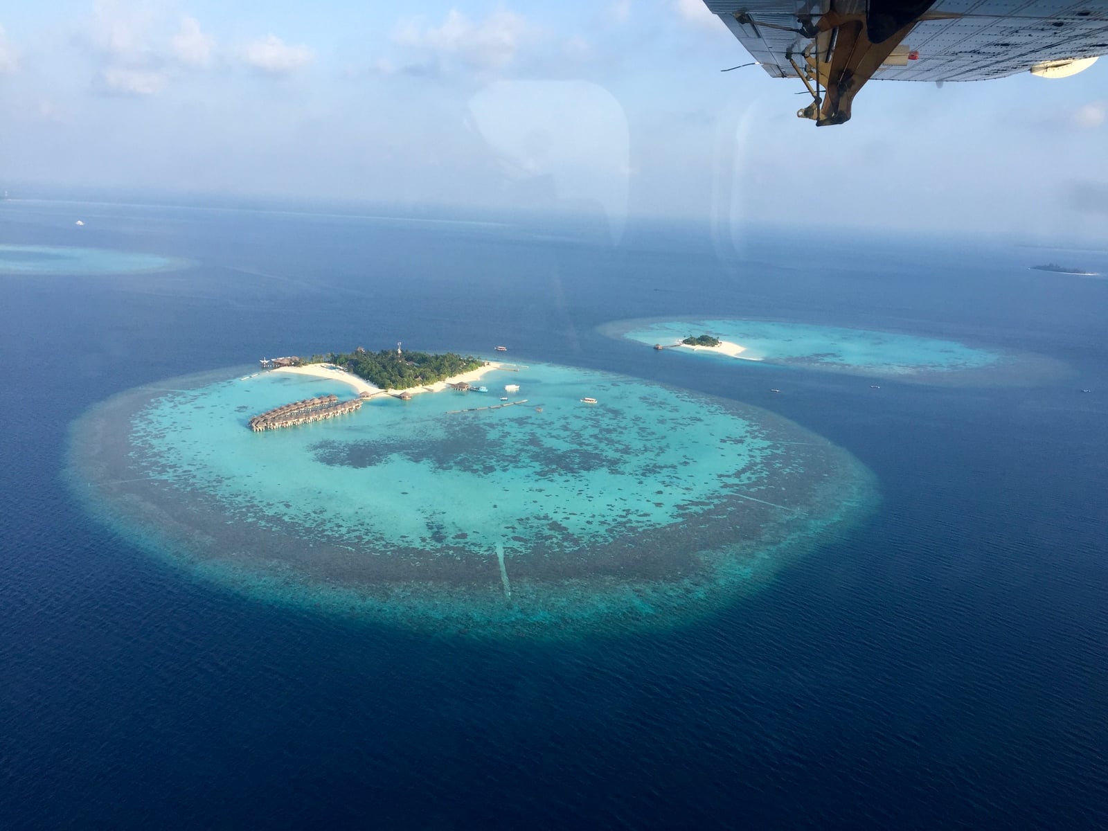 View of a Maldives island from a seaplane window, with overwater villas curving along a turquoise lagoon