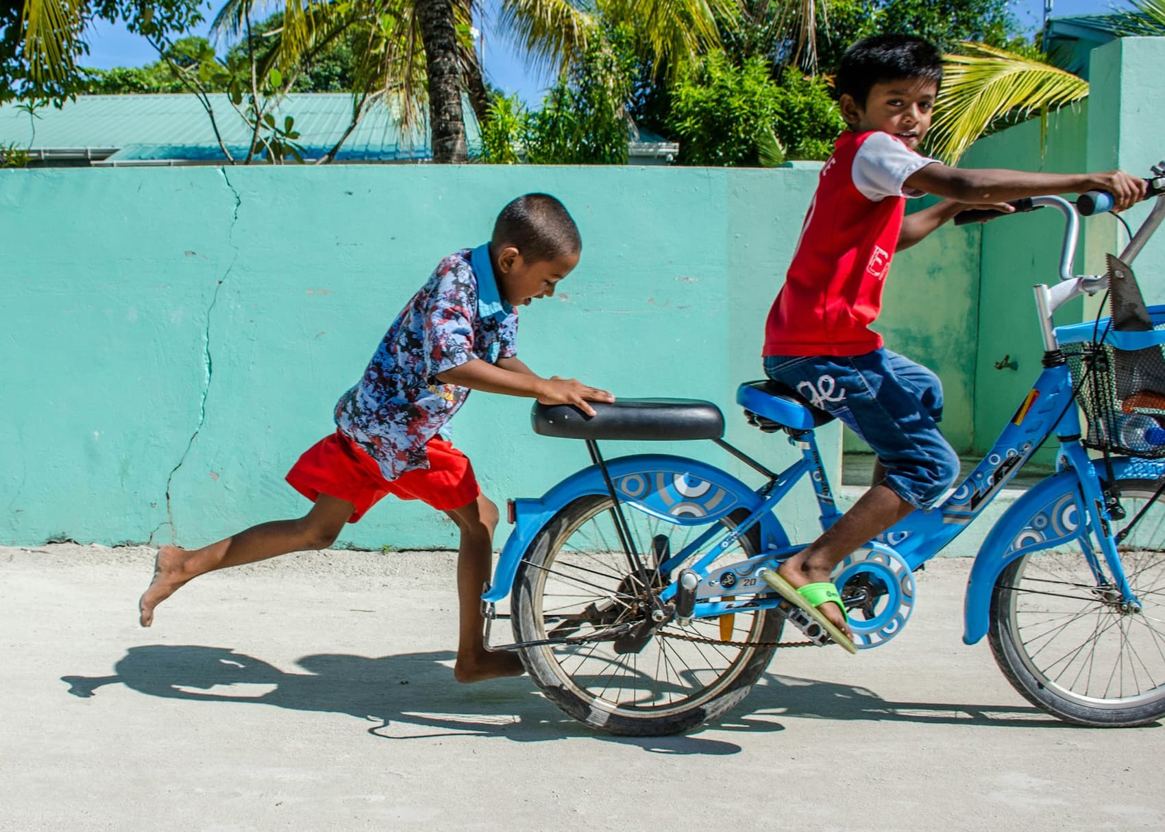 Two Maldivian boys playing with a bicycle on a local-island street