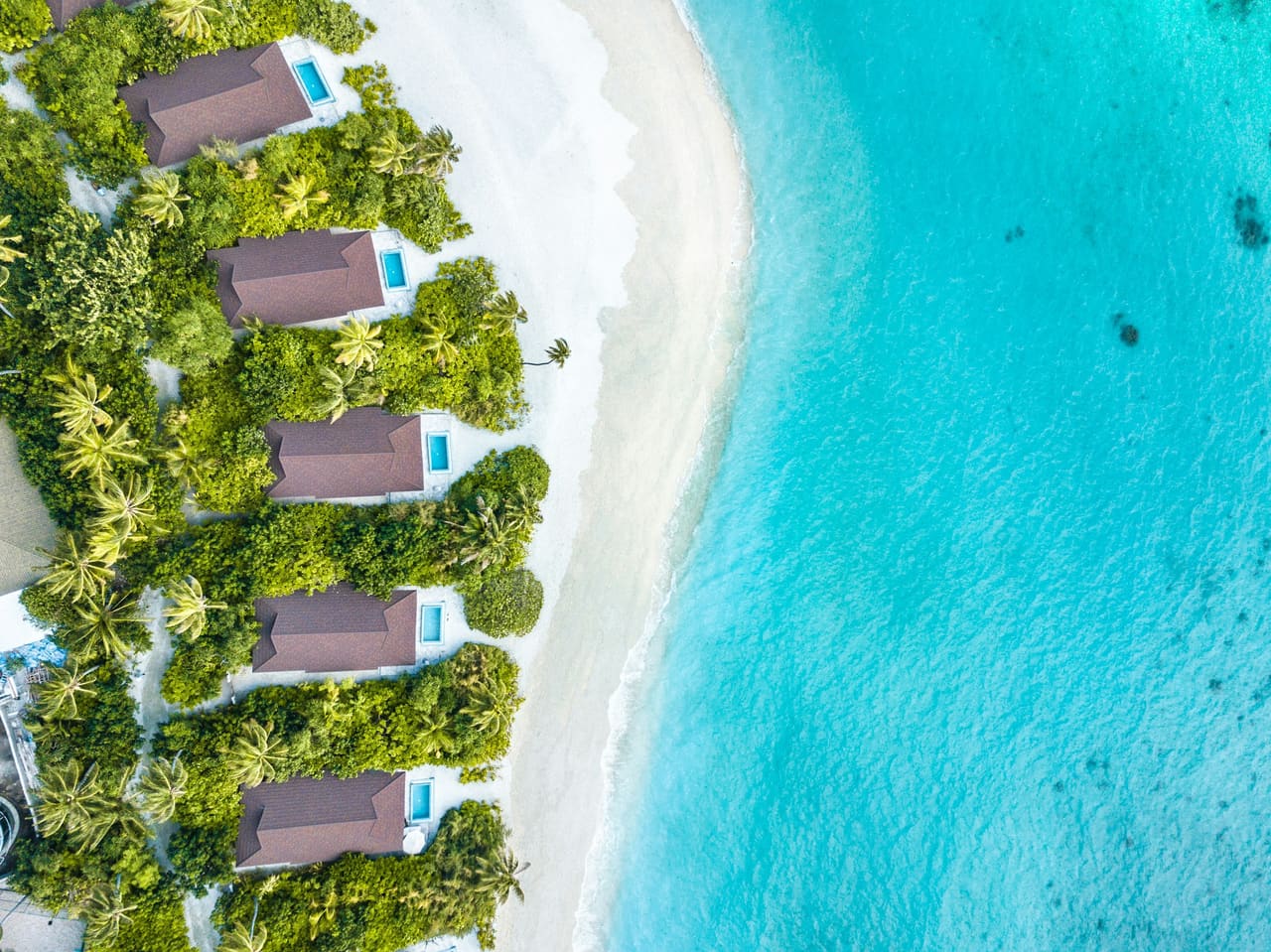 Vista aerea di beach villa con tetto in paglia lungo una spiaggia di sabbia bianca accanto a una laguna turchese maldiviana
