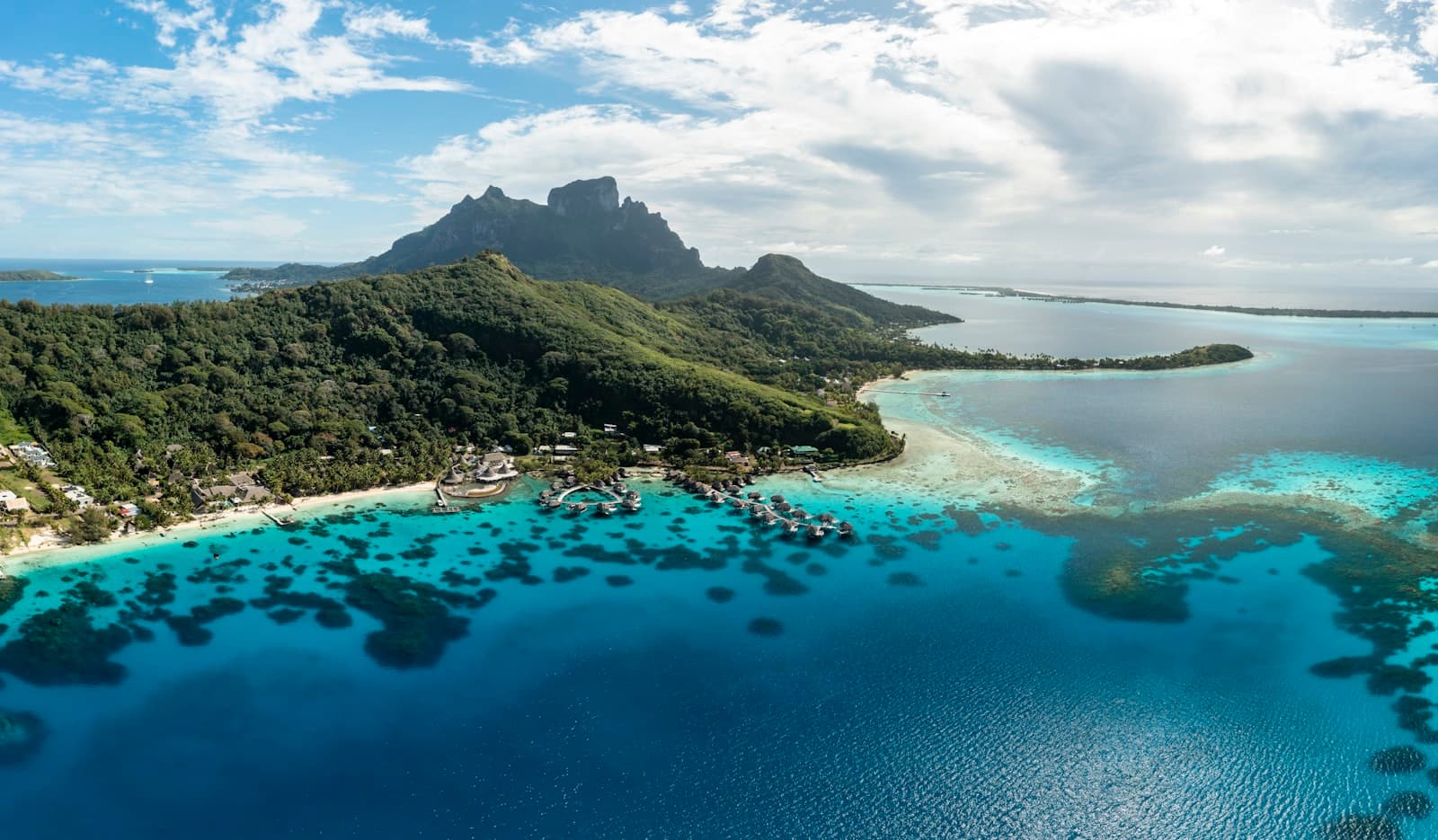 Luftaufnahme des Mount Otemanu auf Bora Bora, der sich über einer türkisfarbenen Lagune mit Wasserbungalows erhebt