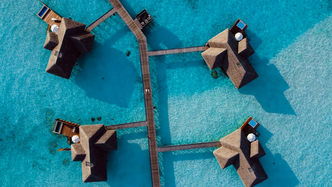 Aerial view of thatched overwater villas linked by boardwalks over a turquoise Maldivian lagoon