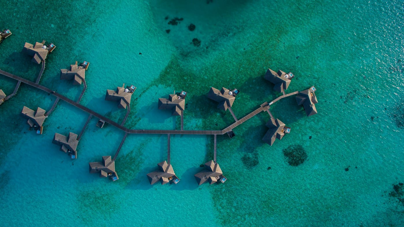 Vue aérienne de villas sur pilotis et de jetées reliées au-dessus d'un lagon maldivien vert-bleu limpide