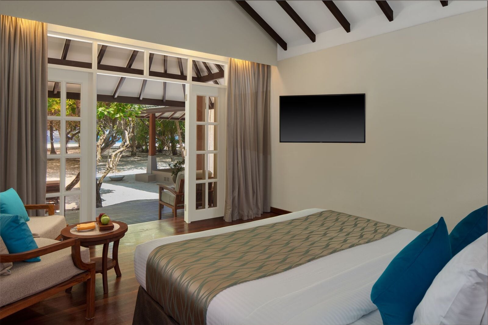 Ein Schlafzimmer mit einem großen Bett, türkisfarbenen Kissen und Glastüren, die auf eine Gartenterrasse führen.