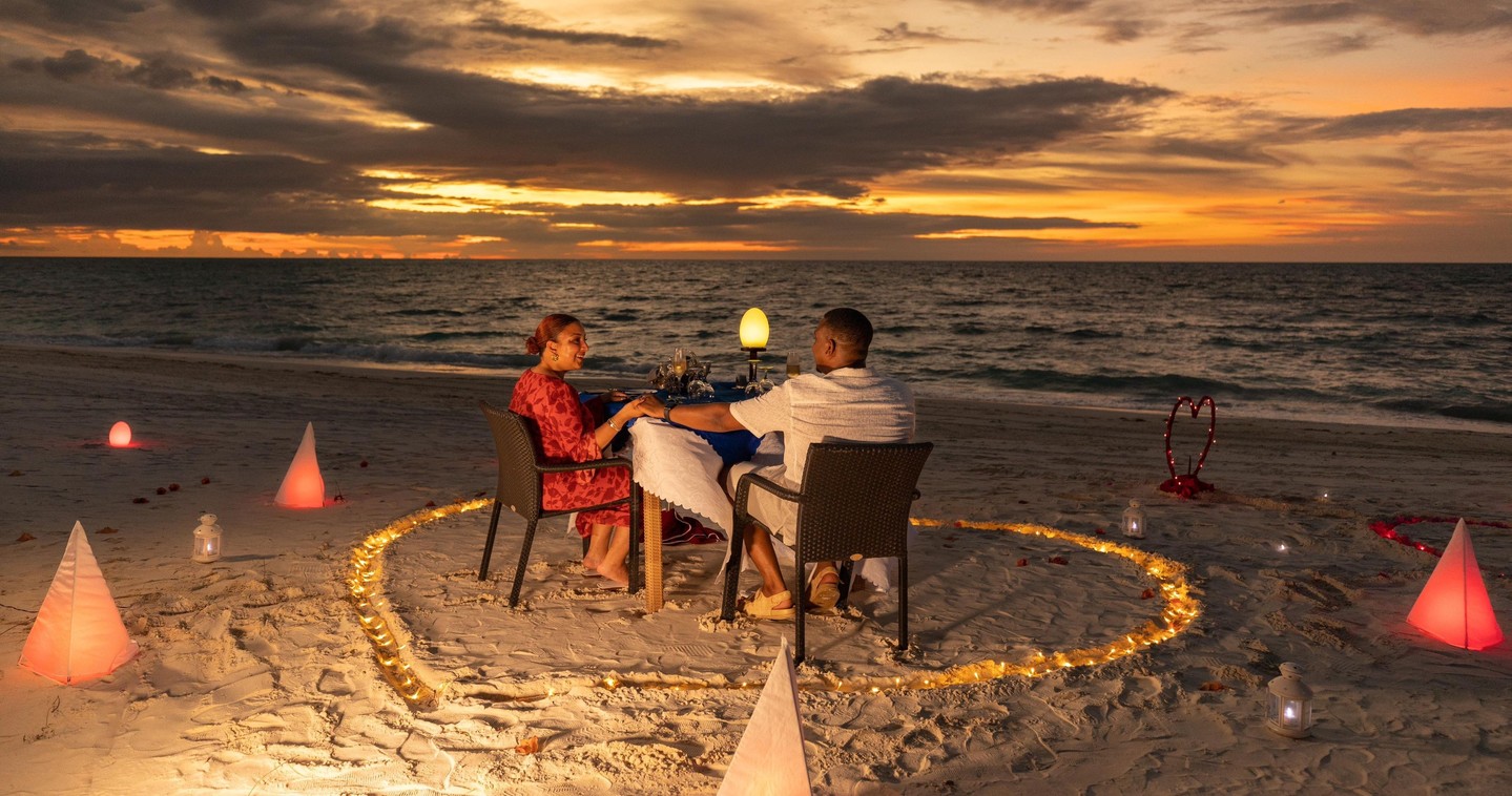 Foto von Atmosphere Kanifushi Maldives vom 13. Juli 2026. Könnte ein Bild von einer oder mehreren Personen, Feuer, Wunderkerze, Liegestuhl, Dämmerung, Strand und Text sein.