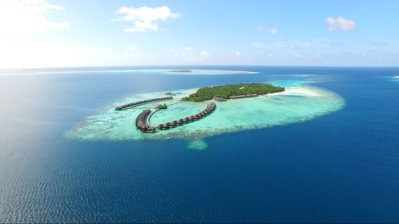 Luftaufnahme einer üppigen Insel bei Ayada Maldives, umgeben von türkisfarbenem Riff und Wasservillen.