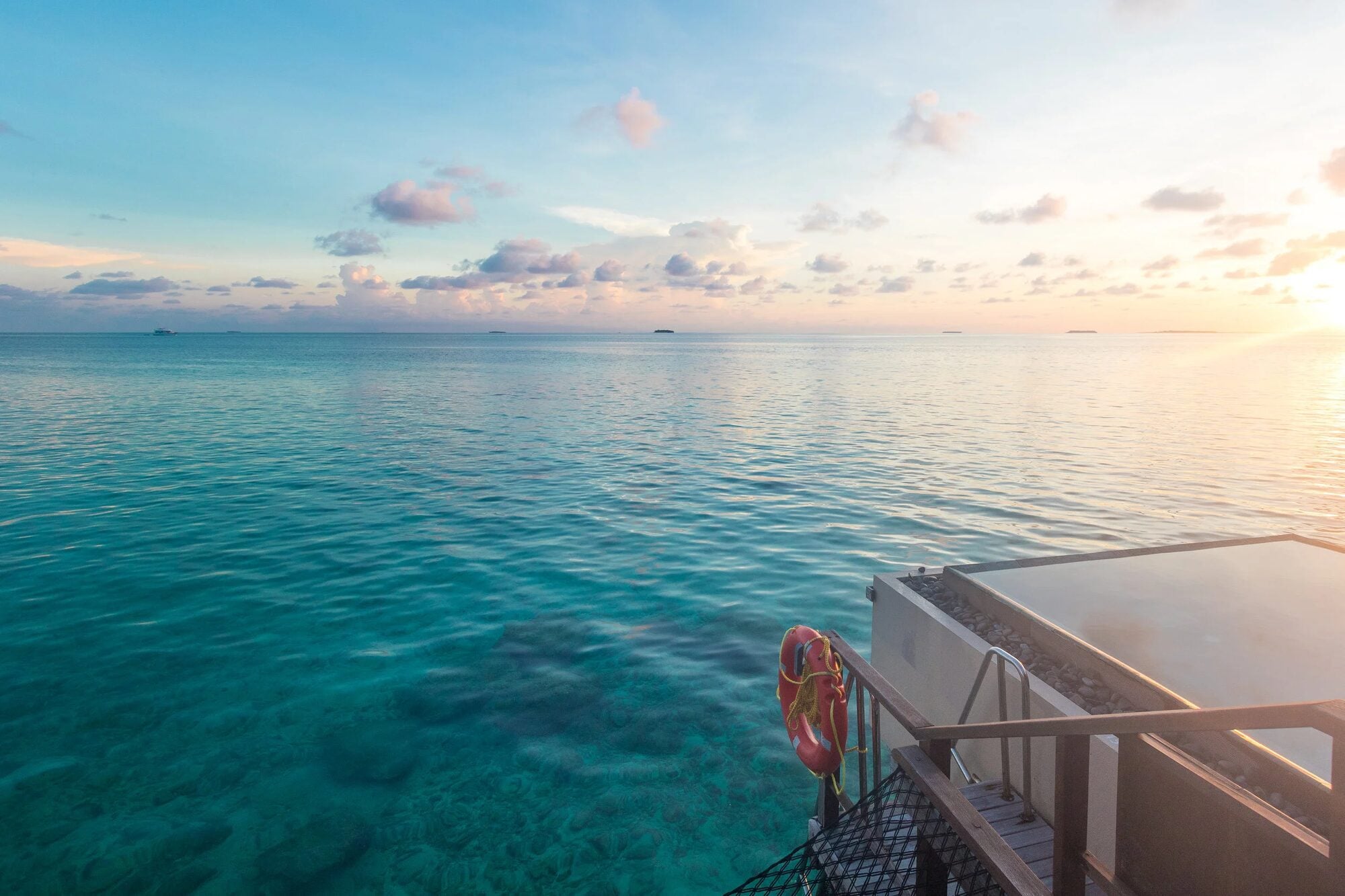 Blick von einem Deck über dem Wasser auf die ruhige Lagune bei Sonnenuntergang, mit einem Rettungsring im Vordergrund.