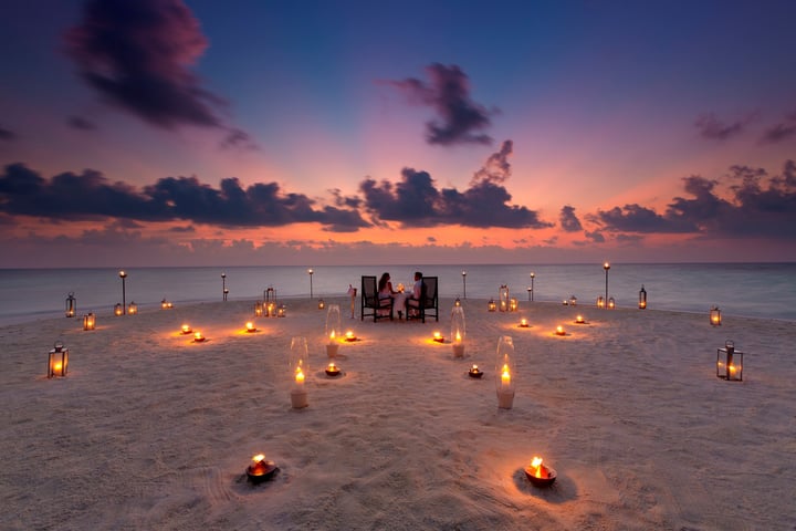 Photo by Baros Maldives on June 14, 2026. May be an image of one or more people, fire, lantern, candle, twilight, beach, water and text.