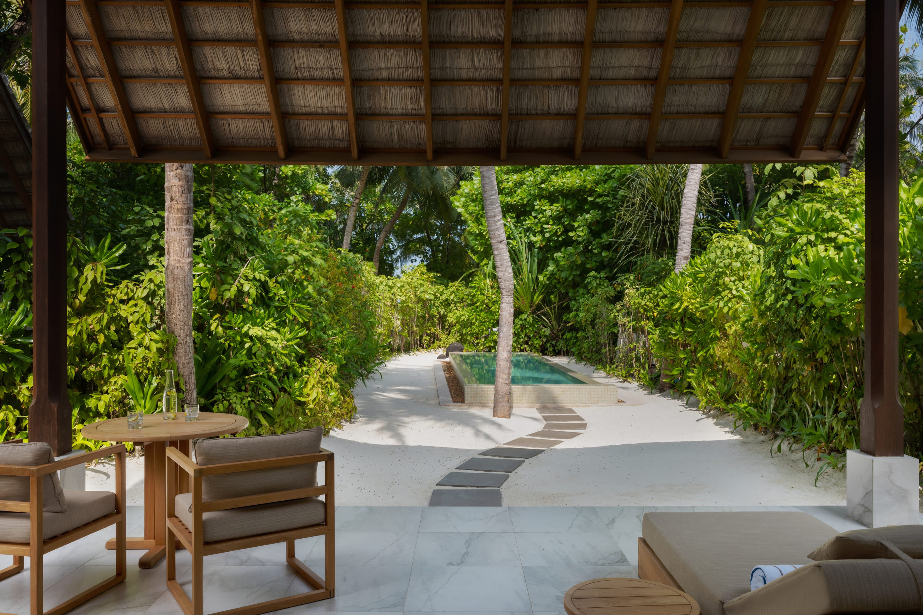 Außensitzbereich mit Tisch, Stühlen und Weg zum Pool im Conrad Maldives Rangali Island