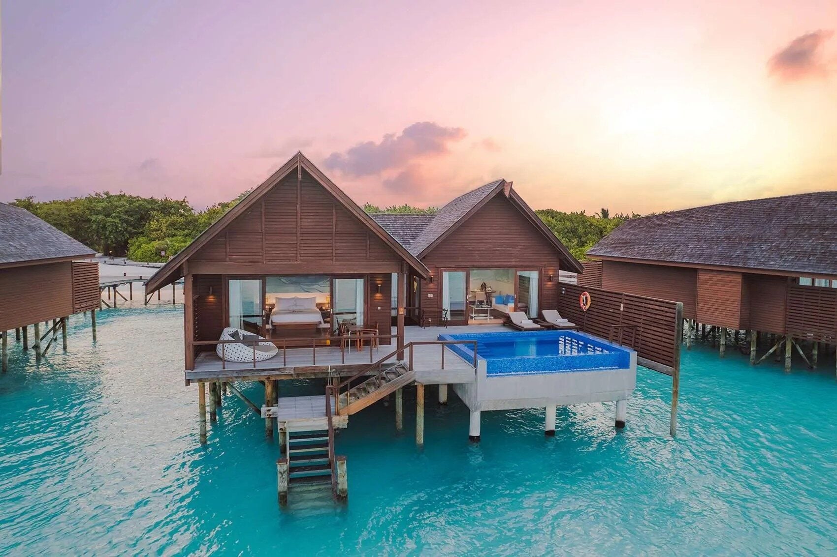 Luftaufnahme von Wasservillen mit privaten Plunge Pools über einer türkisfarbenen Lagune bei Sonnenuntergang.