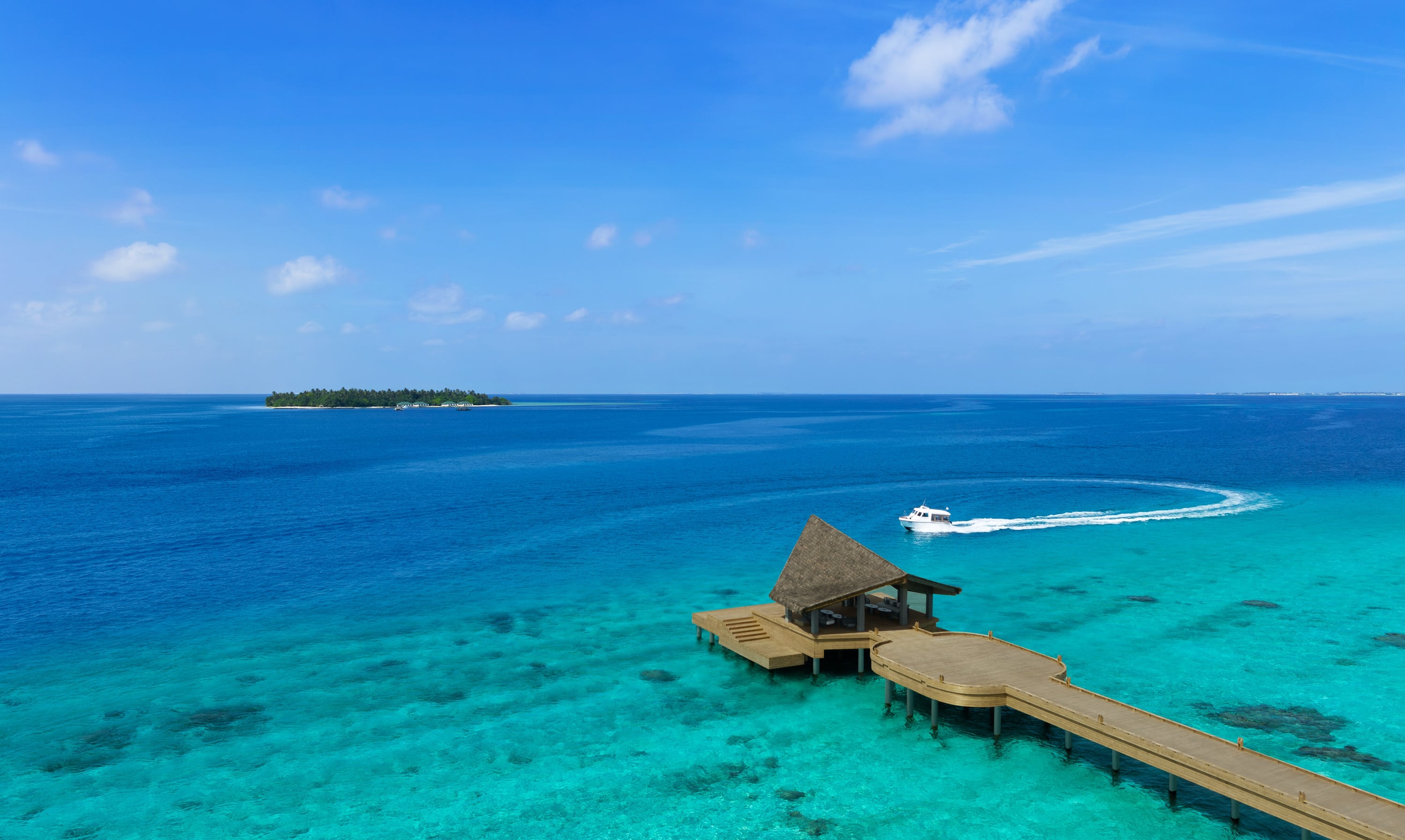 A thatched arrival pavilion at the end of a long timber jetty over turquoise water, with a speedboat curving in.