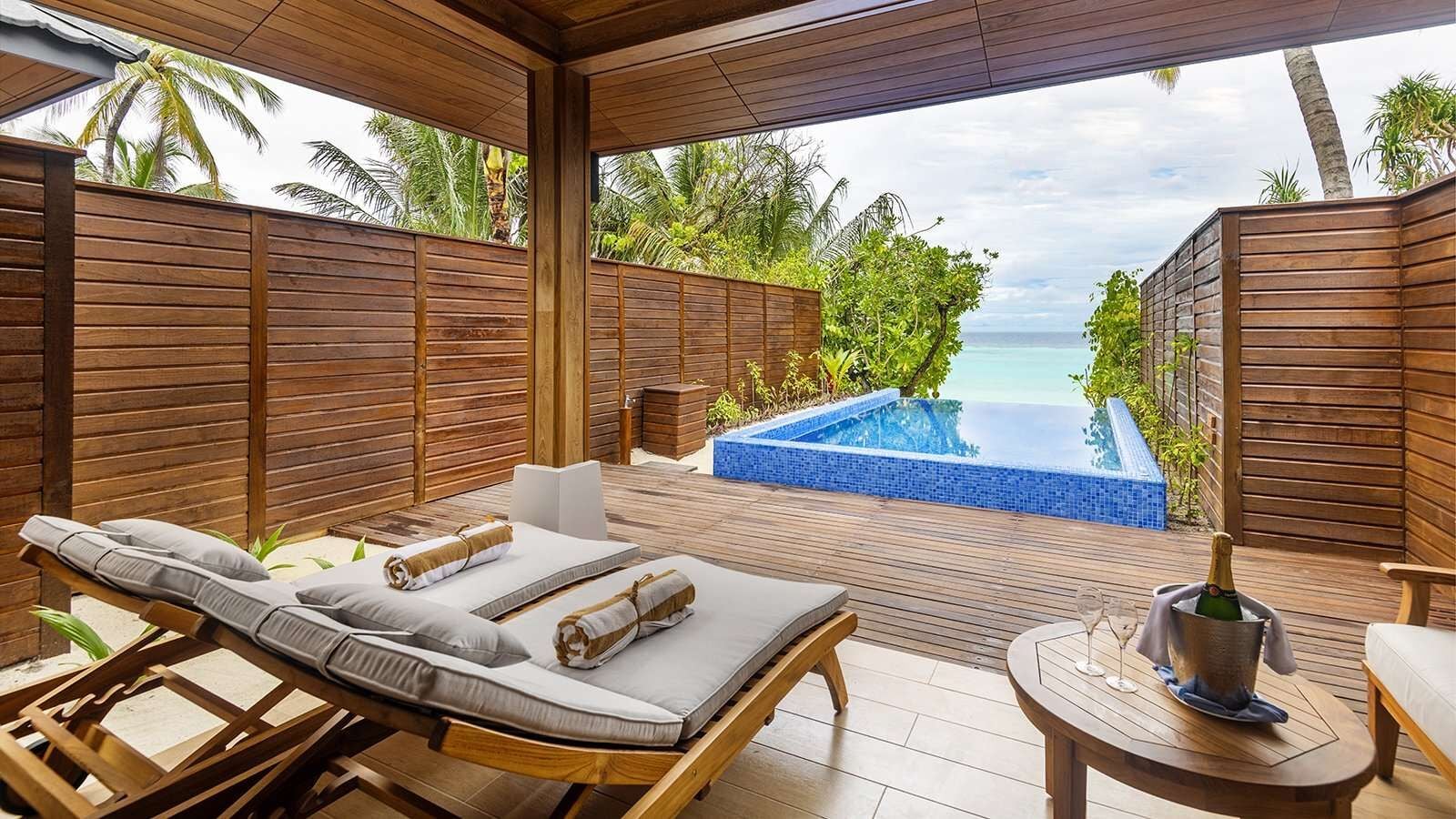 Eine Holzterrasse mit Sonnenliegen und Champagner neben einem privaten Plunge Pool mit Meerblick.