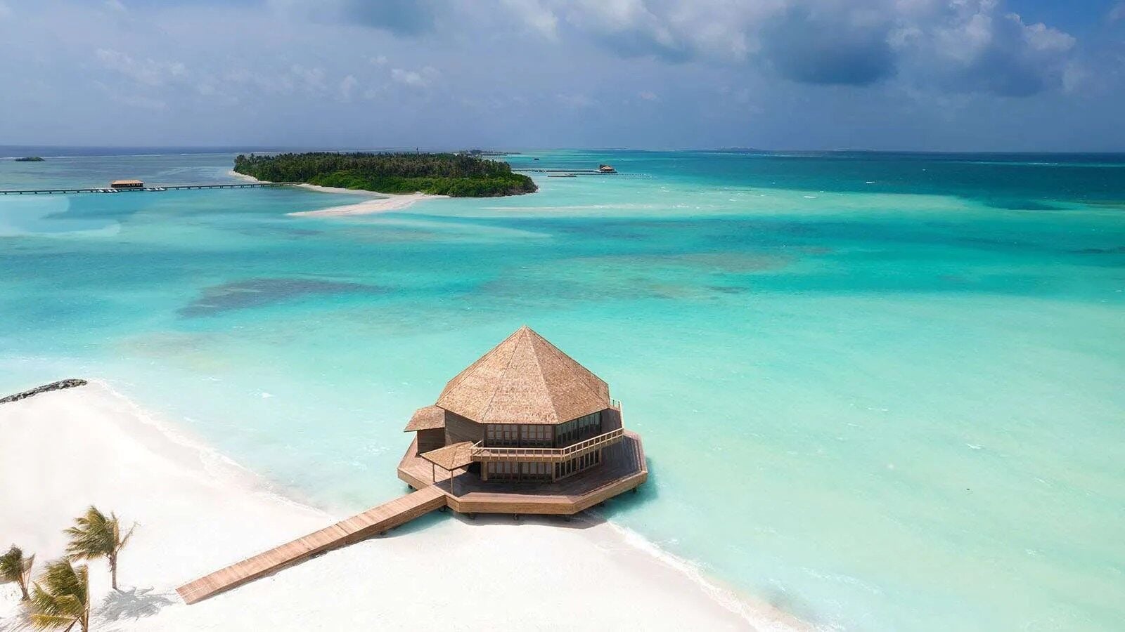 Luftaufnahme eines überwasserpavillons mit Reetdach, umgeben von türkisfarbenem Lagunenwasser.