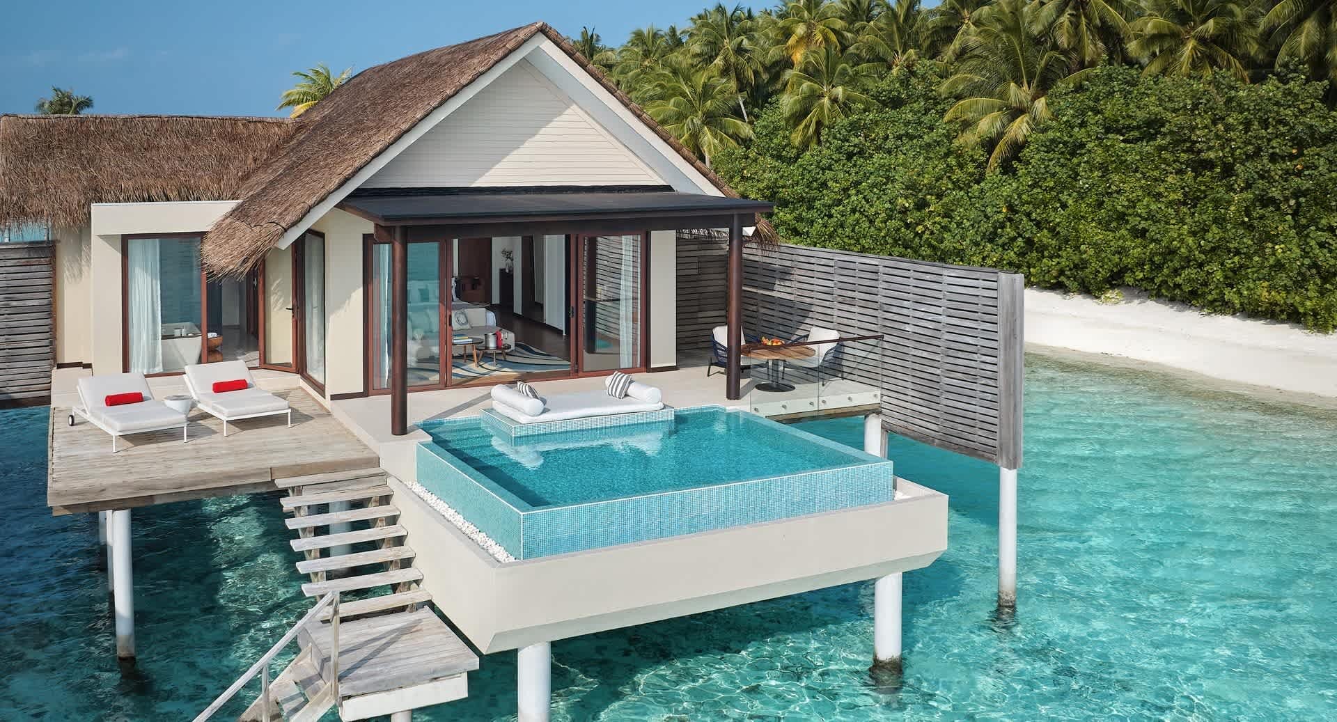 Eine Wasservilla mit privatem Plunge-Pool steht auf Stelzen über einer türkisfarbenen Lagune, im Hintergrund Palmen.