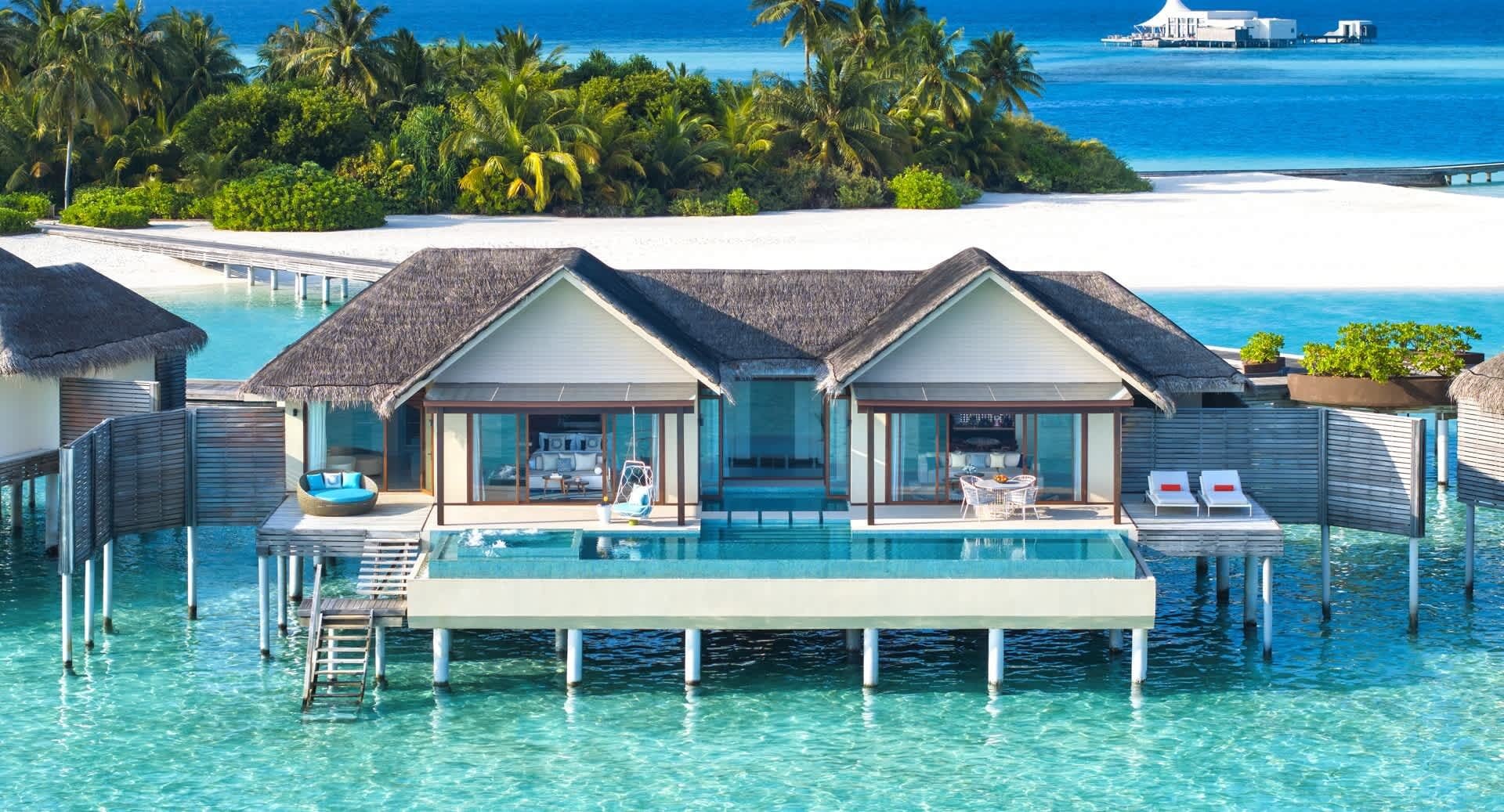 Zwei strohgedeckte Wasservillen mit privaten Pools sind über eine Holzterrasse miteinander verbunden und liegen über der Lagune.