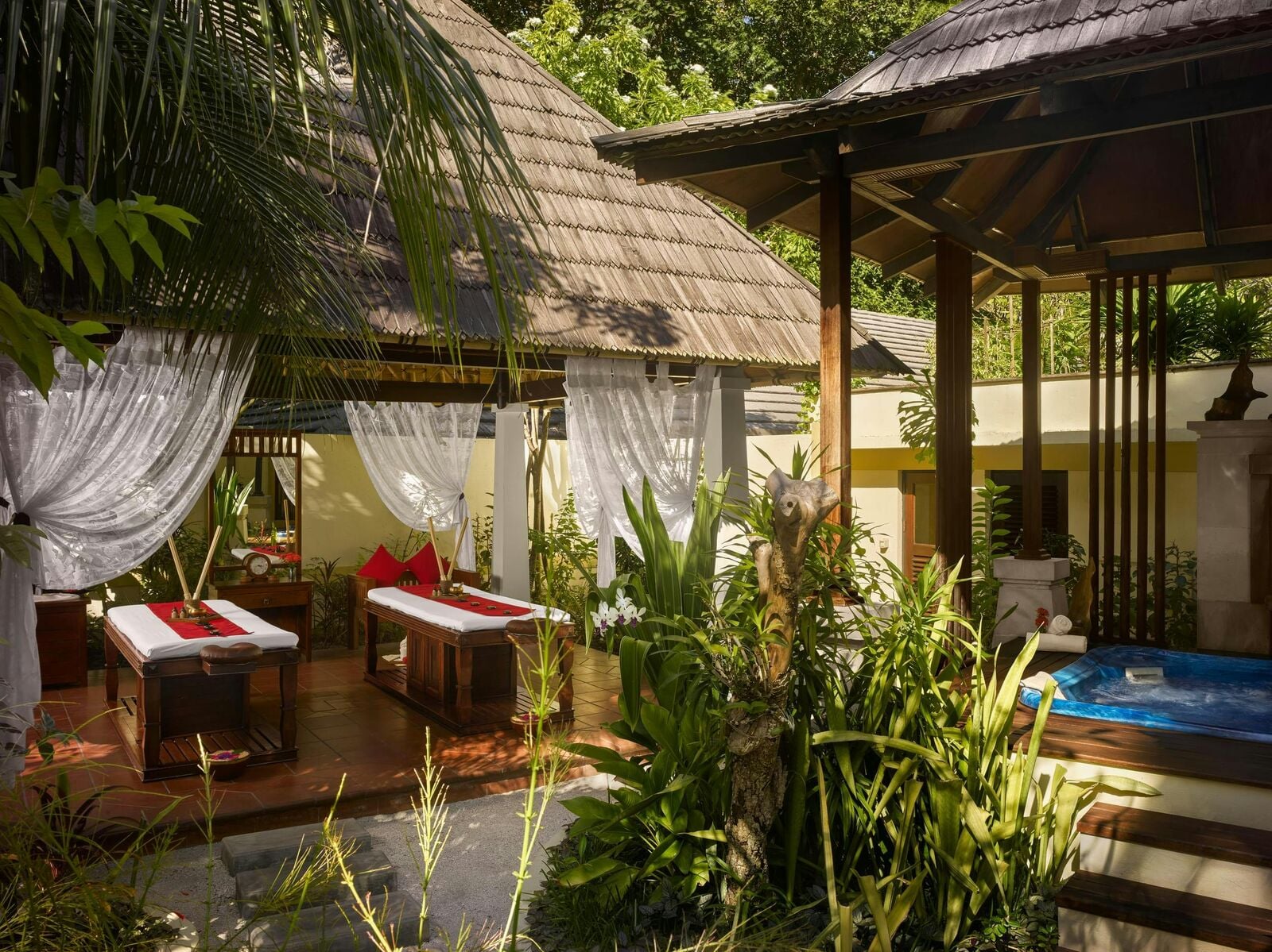 Zwei Massageliegen stehen unter einem Baldachin in einem üppigen Gartenbereich, in dessen Nähe sich ein Plunge Pool im Royal Island Resort befindet.