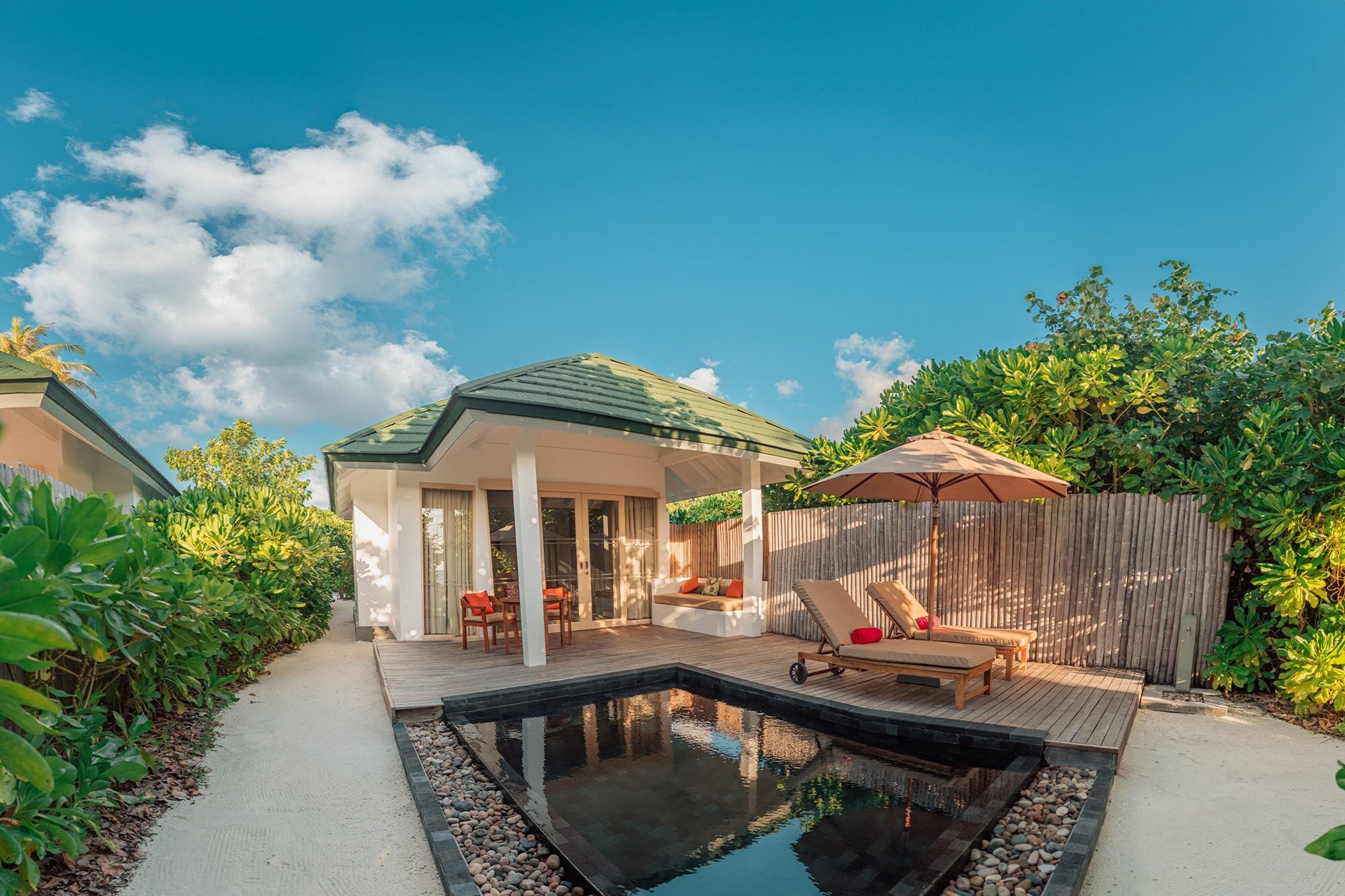 Eine Strandvilla mit spitzem Dach liegt neben einem privaten Tauchbecken, umgeben von Liegen und einem Sonnenschirm im Siyam World Maldives.