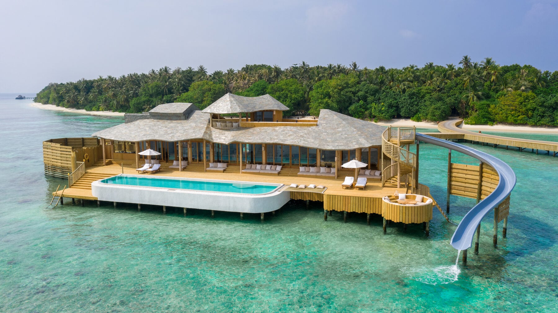 Luftaufnahme einer Wasservilla mit privatem Pool und einer spiralförmigen Wasserrutsche, die in die Lagune führt.