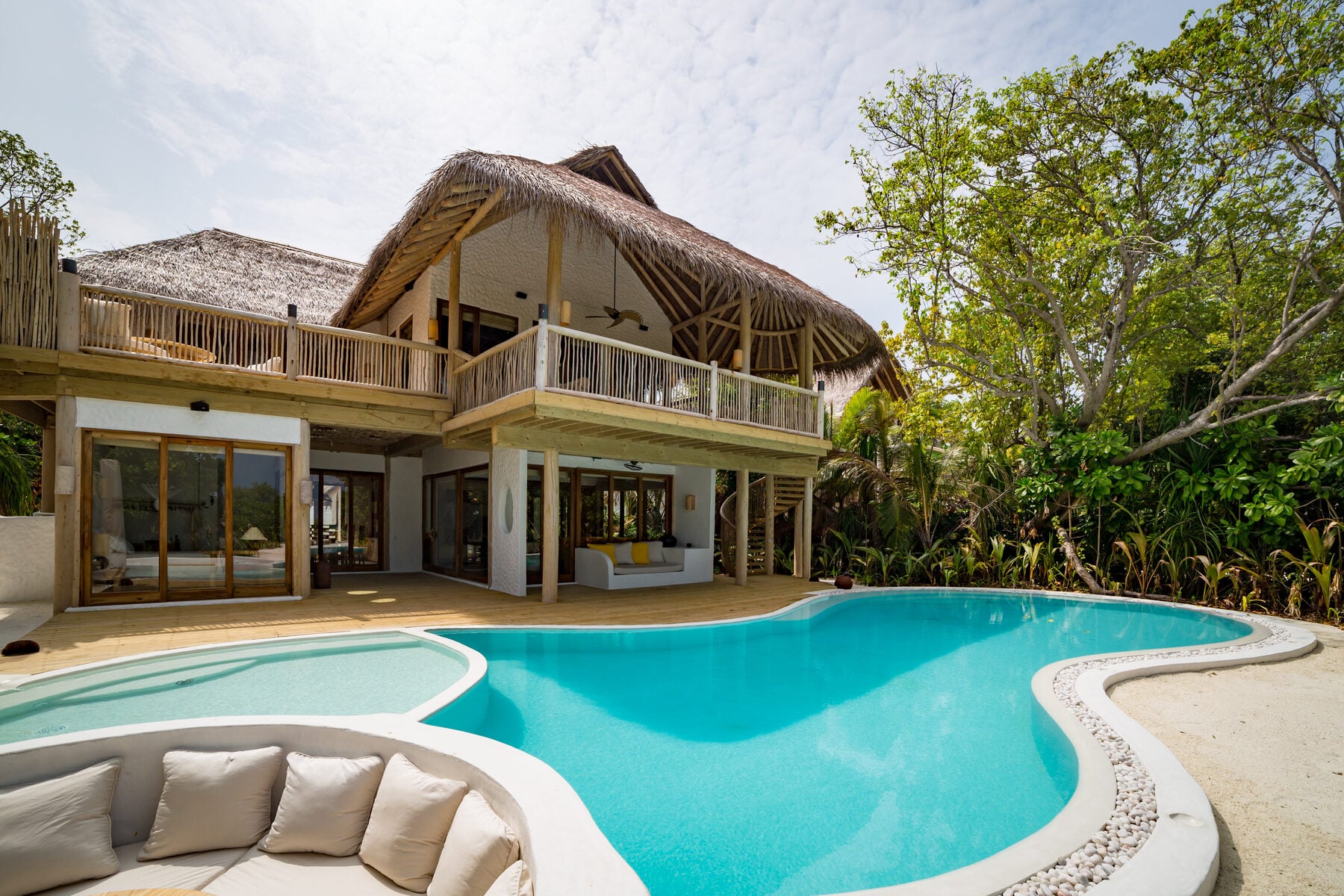 Zweistöckige Villa mit Reetdach, geschwungenem Pool und Loungebereich, umgeben von tropischem Grün.