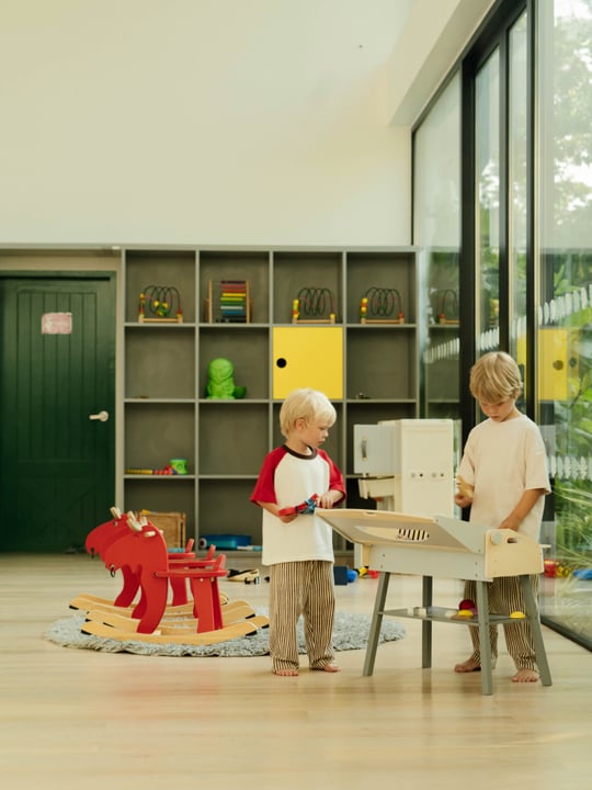 Due bambini che giocano insieme all'interno del Park Players Kids' Club di Villa Park, alle Maldive, uno spazio famiglia interno luminoso con giochi, attività e vegetazione tropicale visibile all'esterno.