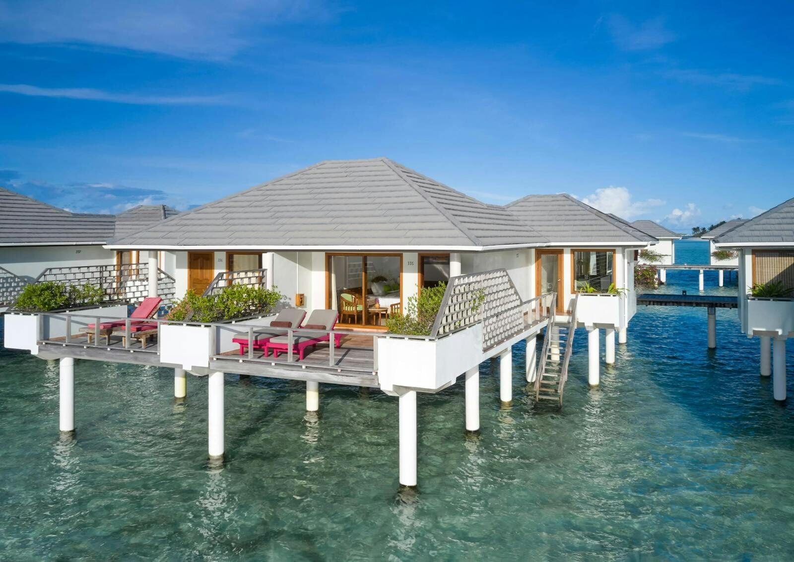 Una water villa a Sun Island si erge su palafitte sopra le acque turchesi della laguna, con lettini prendisole sulla terrazza.