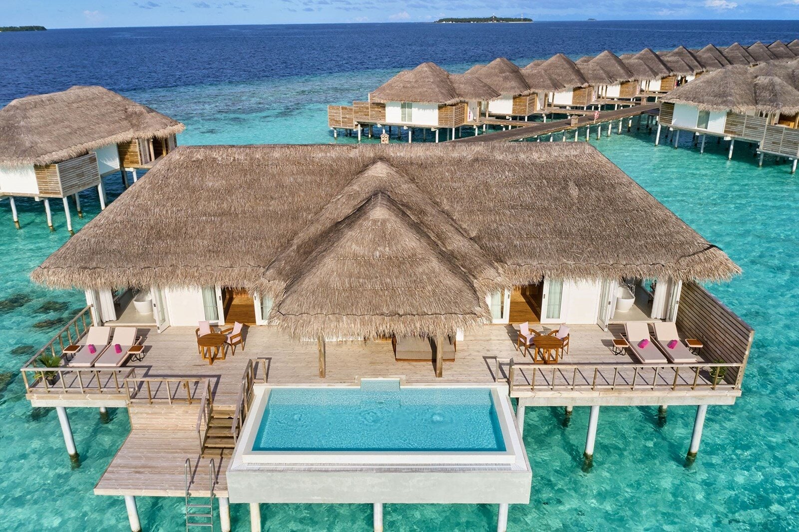 Luftaufnahme strohgedeckter Wasservillen mit privatem Pool, umgeben von türkisfarbener Lagune bei Sun Siyam Iru Veli.