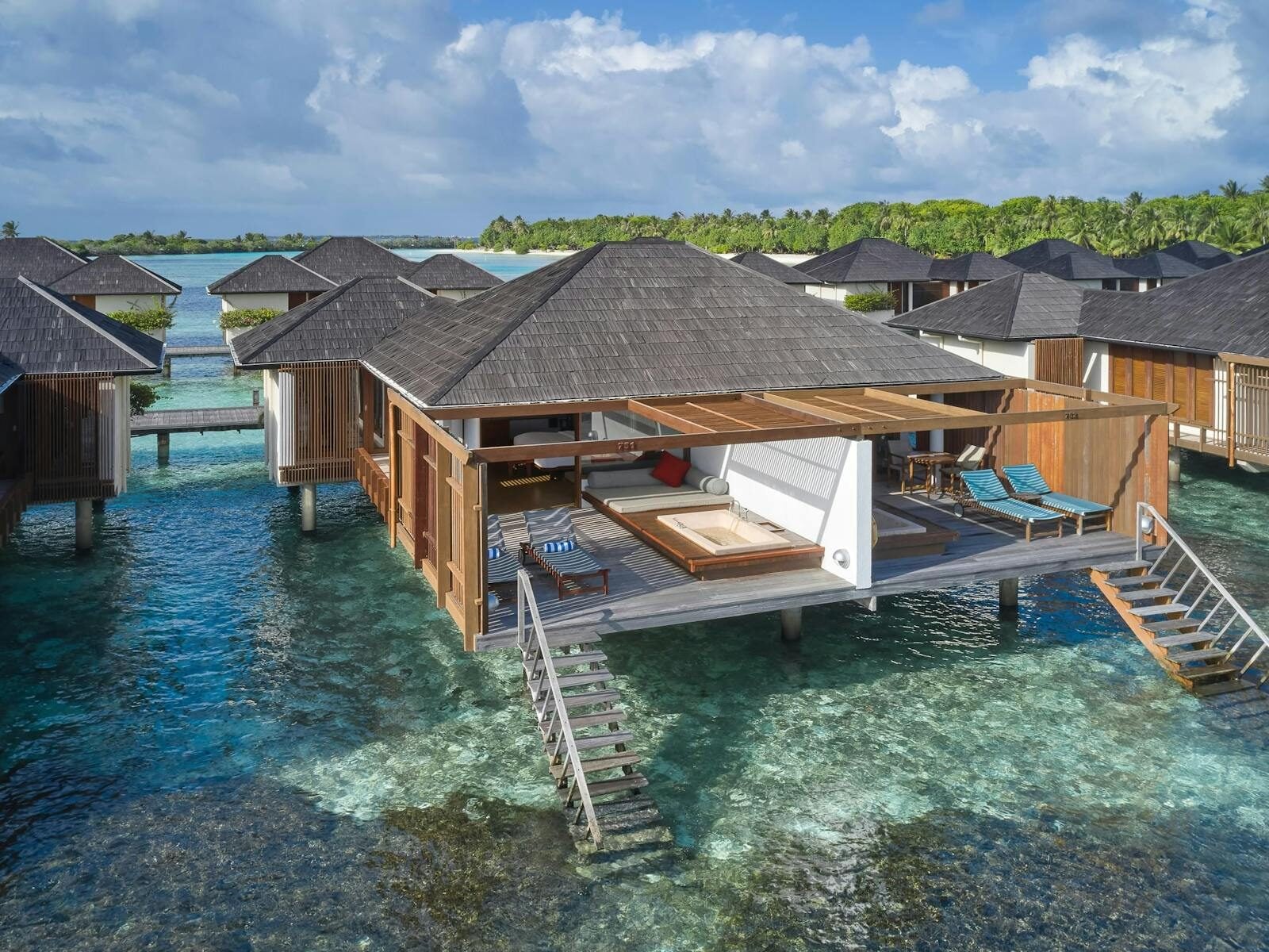 Eine Luftaufnahme zeigt eine Wasservilla mit einer Holzterrasse und Stufen, die in die klare Lagune führen.